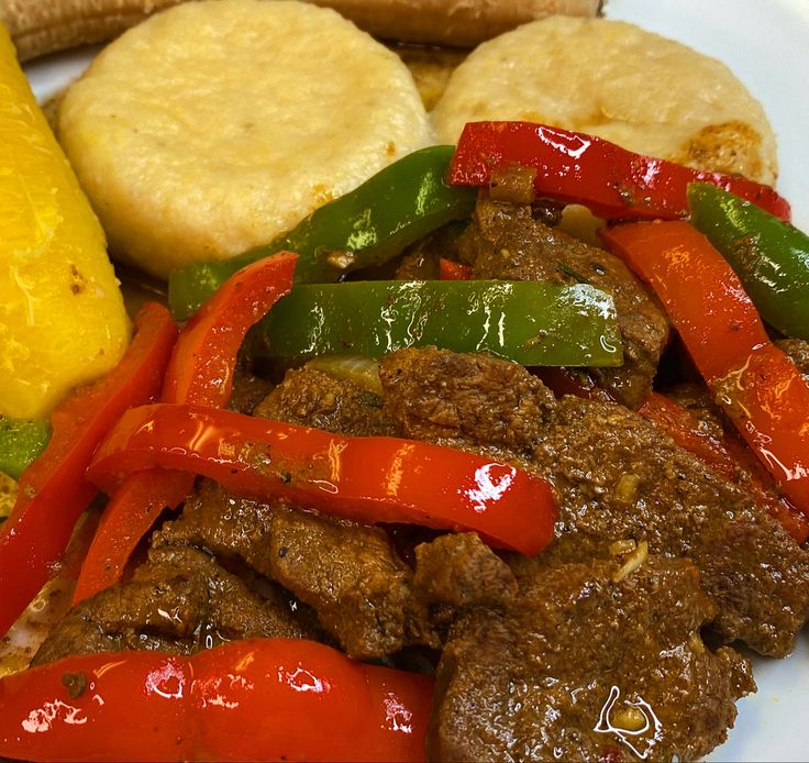 a white plate topped with meat and veggies next to corn on the cob