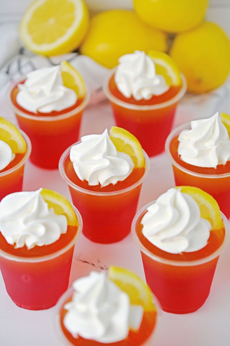 orange jello cups with whipped cream on top and fruit in the background, ready to be eaten