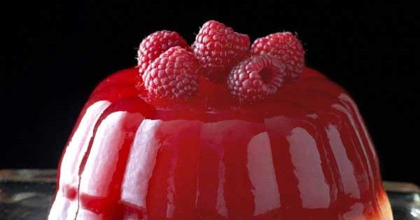 a cake with raspberries on top is sitting on a glass plate and has red sauce