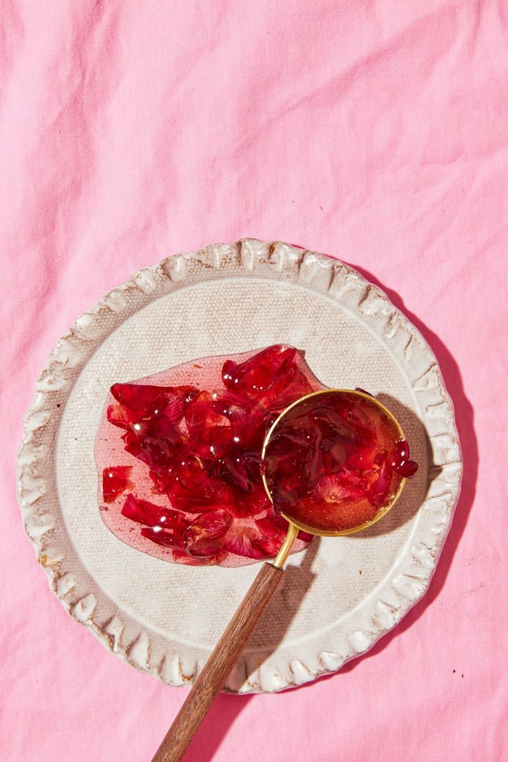 a spoon with some food on it sitting on a paper plate next to a pink cloth