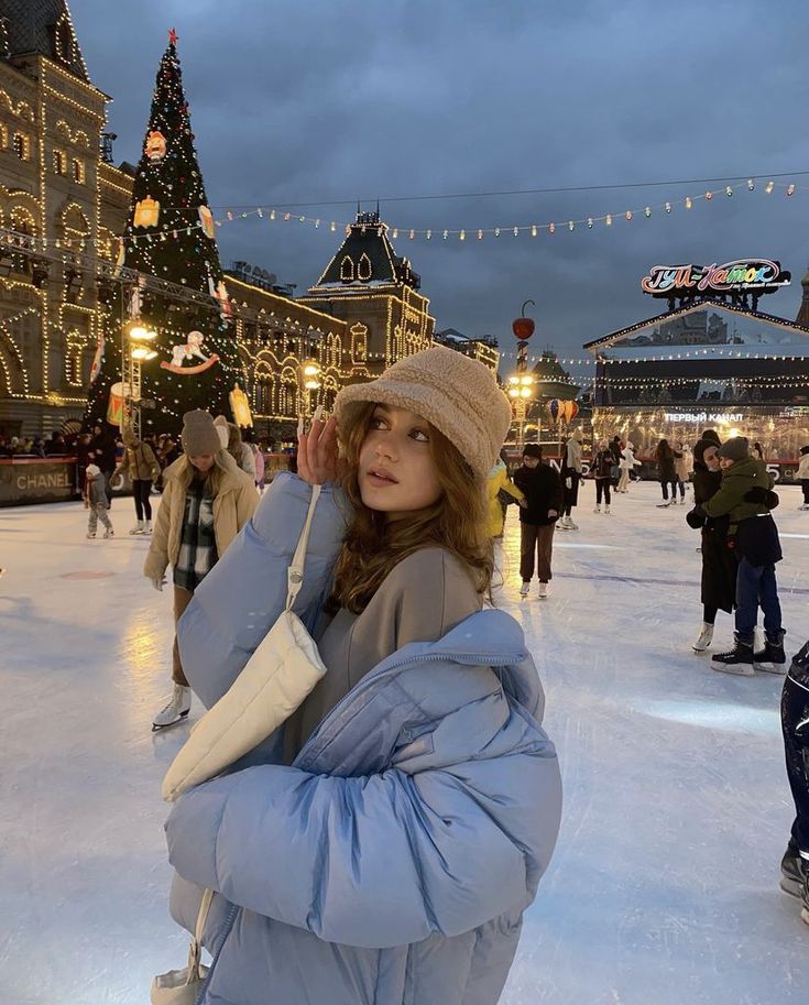 a woman standing on top of an ice covered rink next to a building with christmas lights