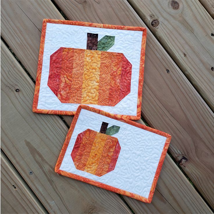 two quilted pumpkins sitting on top of a wooden table