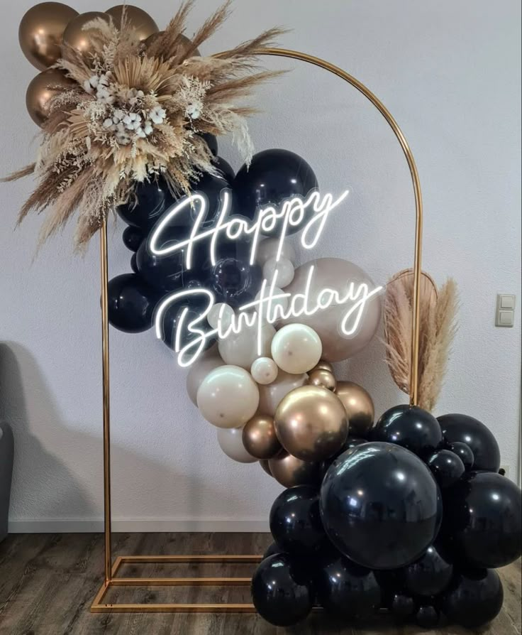 a happy birthday sign surrounded by black and gold balloons