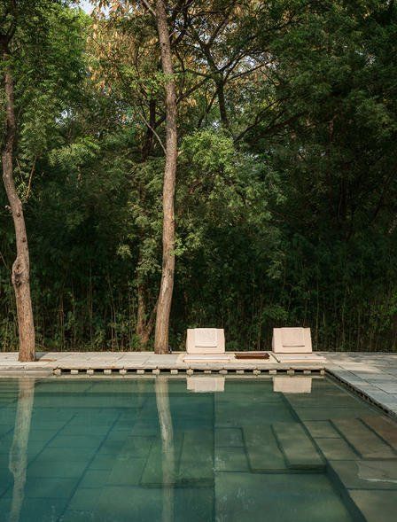 an empty swimming pool surrounded by trees in the middle of a wooded area with lounge chairs