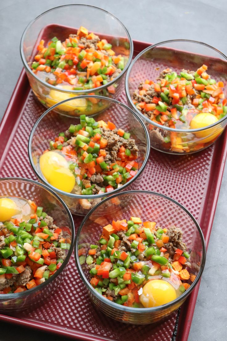 four glass bowls filled with food on top of a red serving tray next to an egg