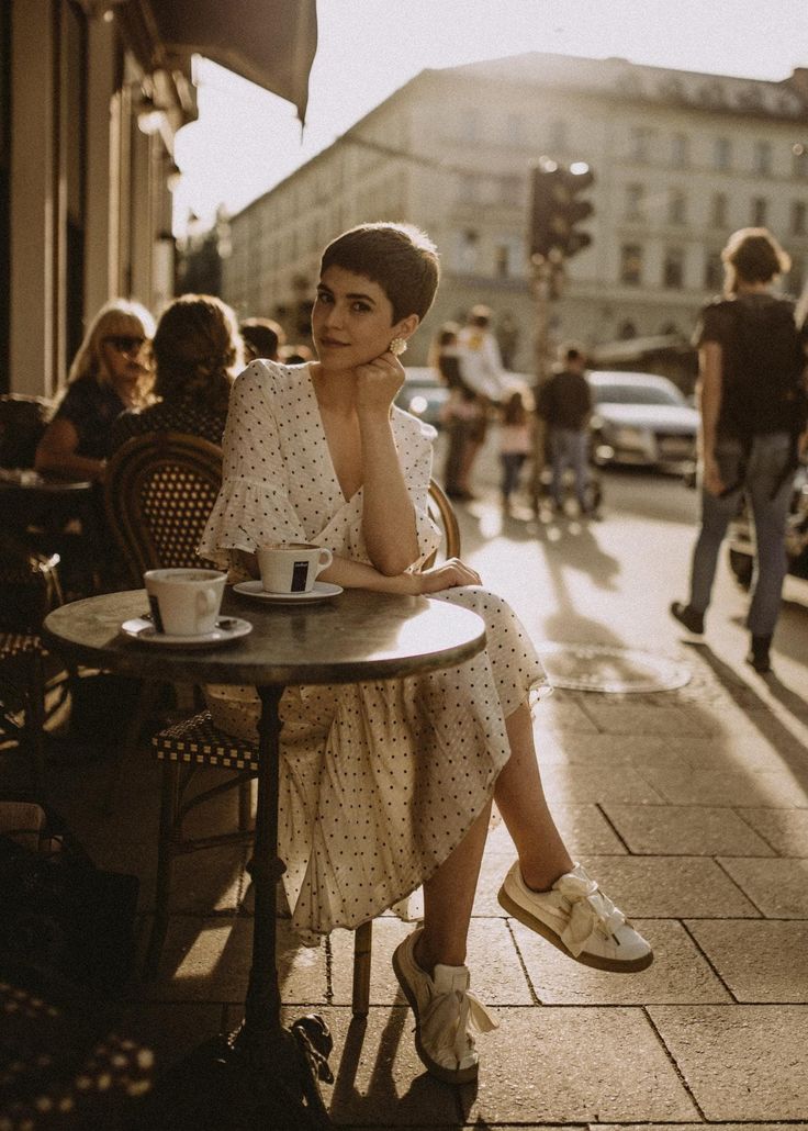 a woman sitting at a table with a cup of coffee in front of her on the sidewalk