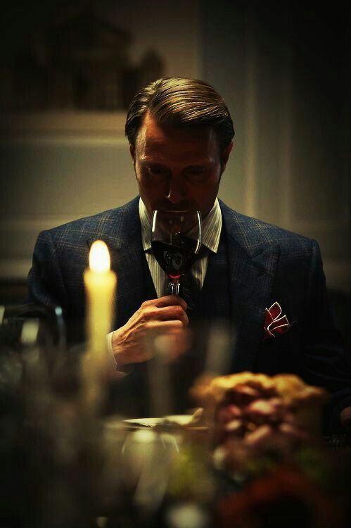 a man sitting at a dinner table holding a wine glass in front of his face