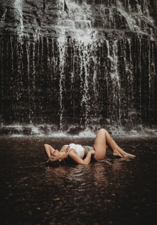 a woman laying on the ground in front of a waterfall with water falling from it