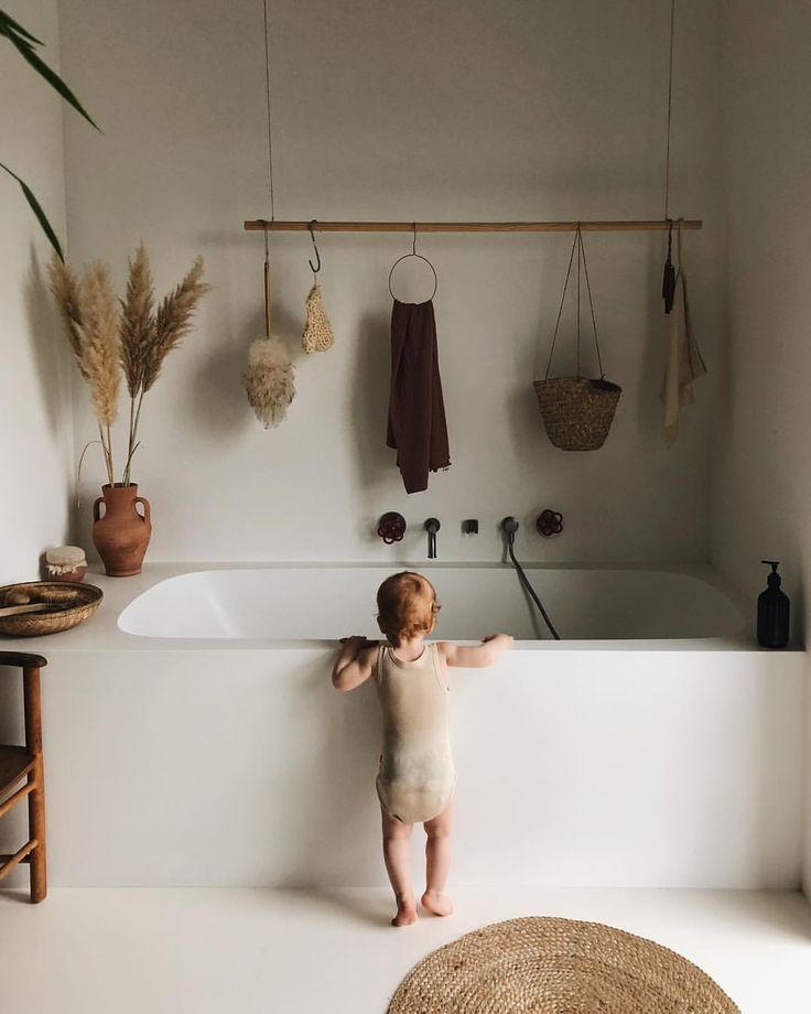 a baby standing on the edge of a bathtub in front of a white wall