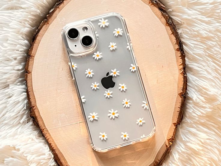 an iphone case with daisies on it is sitting on a wood slice in front of a white background