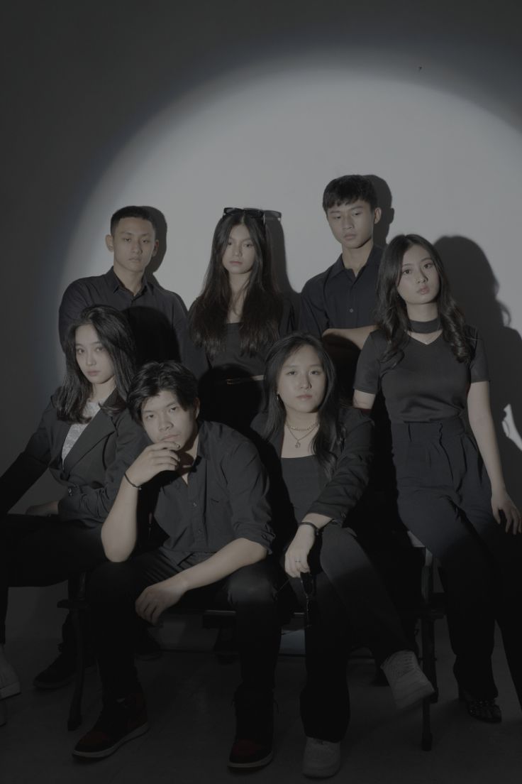 a group of people sitting next to each other in front of a white wall with shadows on it