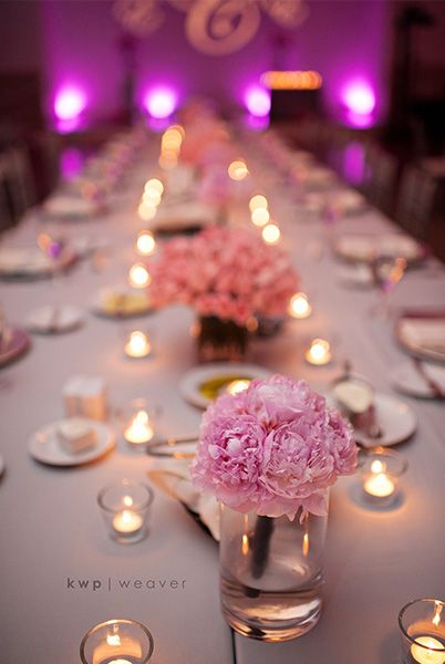 a long table with candles and pink flowers in vases on the center, surrounded by plates