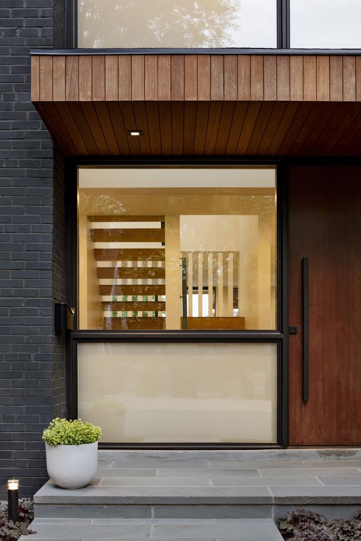 the entrance to a modern home with wood and glass doors, stone steps and potted planter