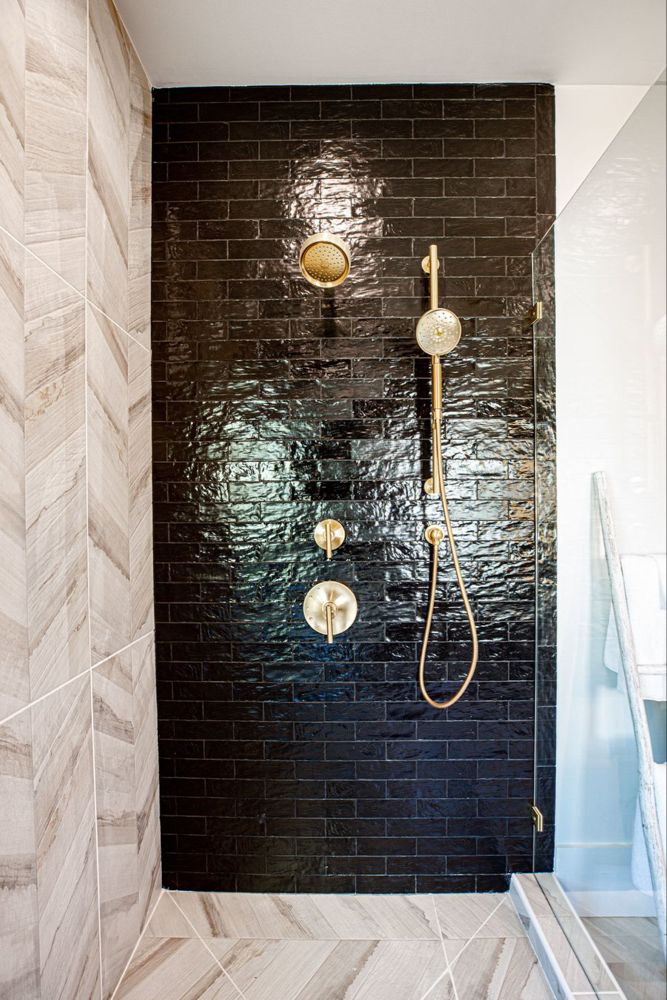 a bathroom with black tile and gold fixtures on the shower head, hand held by a brass faucet