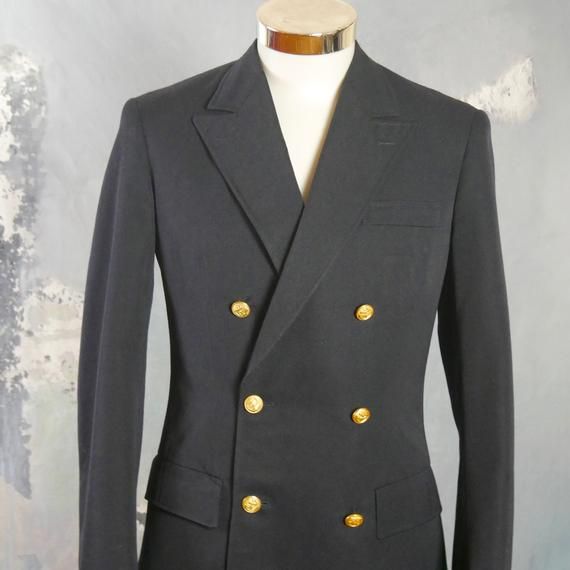 This 1960s German vintage double-breasted naval officer's jacket has peak lapels and padded shoulders, and closes in the front with two gold anchor buttons (six in total show on the front). The handsome blazer has three pockets on the front, and the left chest pocket has small pinholes where a patch was removed. The jacket is lined in a navy blue satin viscose fabric, and has three inner pockets.Brand label: Kleiverfabrik Knab (Germany)Size: 36 US/UKMaterial: 55% polyester, 45% woolCondition: Ex Formal Navy Double-breasted Pea Coat, Navy Double-breasted Blazer With Buttons, Navy Pea Coat With Buttons For Formal Occasions, Navy Peacoat With Buttons For Formal Occasions, Formal Navy Peacoat With Buttons, Navy Formal Pea Coat With Buttons, Navy Double-breasted Peacoat, Gold Double-breasted Blazer With Double Button Closure, Navy Double-breasted Sport Coat For Formal Occasions