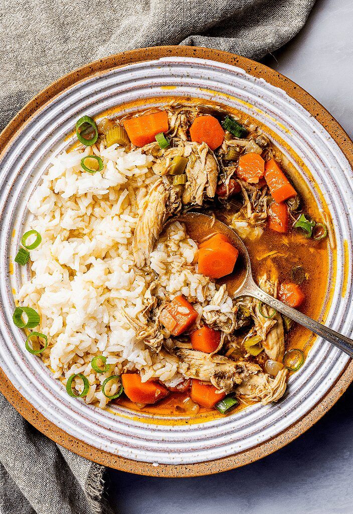 a bowl filled with chicken and rice on top of a white table next to a spoon