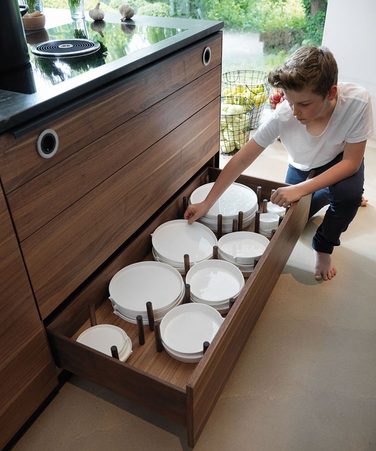 a person kneeling down in front of a drawer filled with white plates and pans