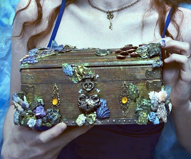 a woman is holding an old trunk with shells on it and jewels in her hands