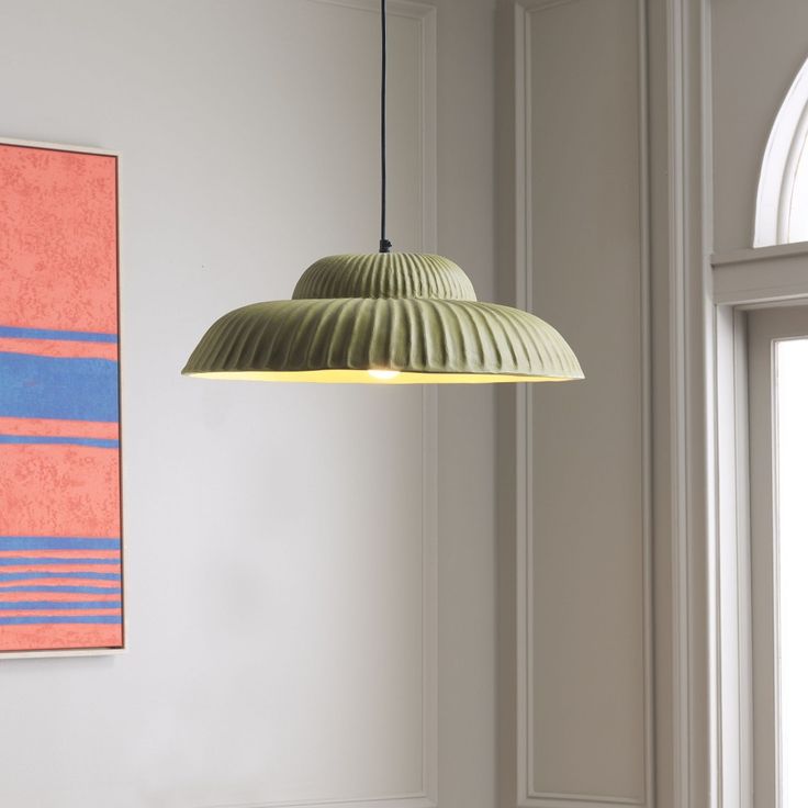 a green lamp hanging from a ceiling next to a painting on the wall in a room