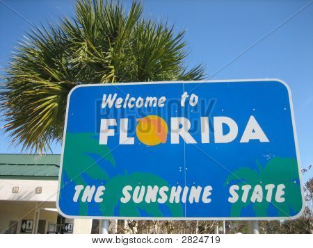 a welcome to florida sign in front of a palm tree and building with blue sky