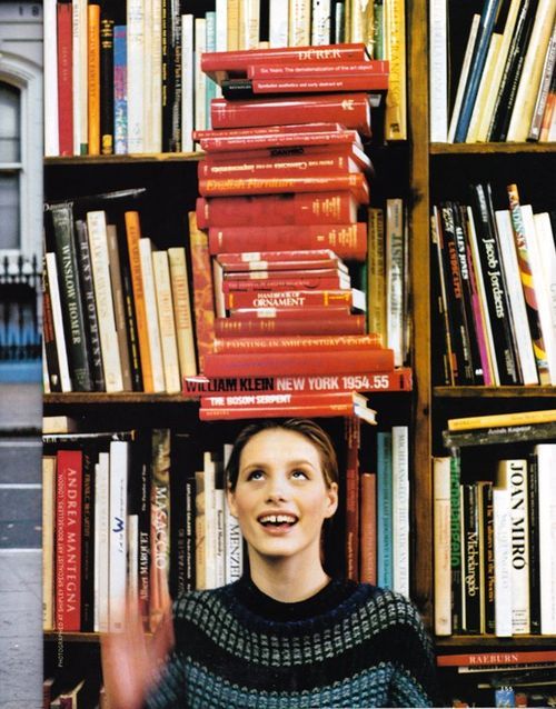 a woman standing in front of a bookshelf with many books on top of her head