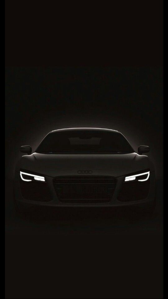 the front end of a black sports car with headlights on in the dark night time