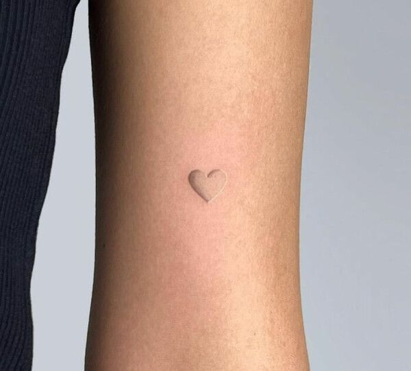 a small heart tattoo on the back of a woman's leg, with her arm behind her