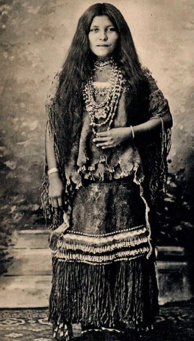 an old black and white photo of a woman in native american dress with long hair