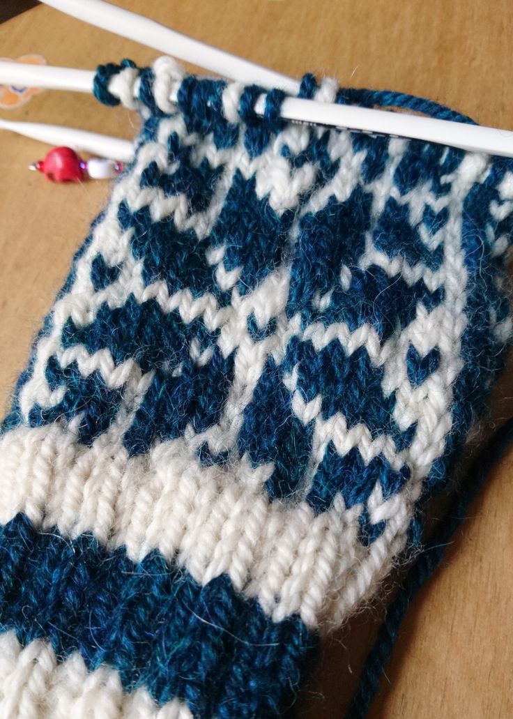 two knitting needles are laying next to a blue and white knitted object on a table