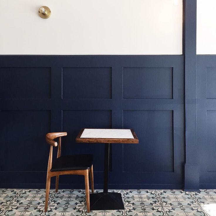 a small table and chair in front of a blue wall with white paneling on it