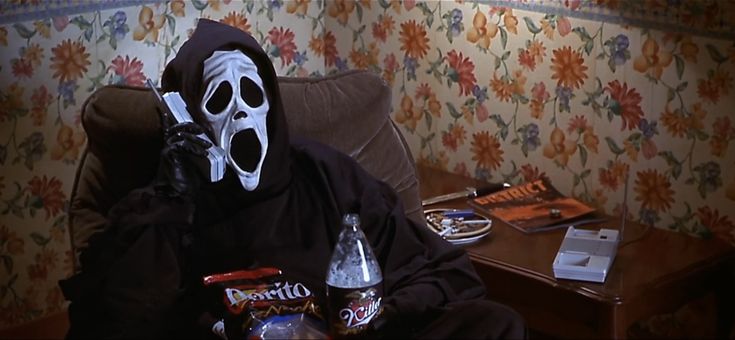 a person in a ghost mask sitting on a couch holding a beer and talking on the phone