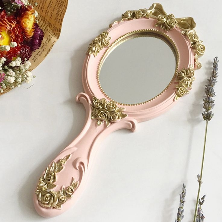 a pink vanity mirror sitting on top of a table next to flowers and a vase