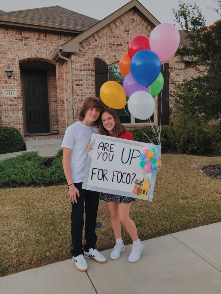 two people standing in front of a house with balloons and a sign that says are you up for food?