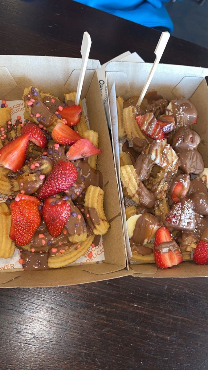 two boxes filled with different types of desserts on top of a wooden table next to each other