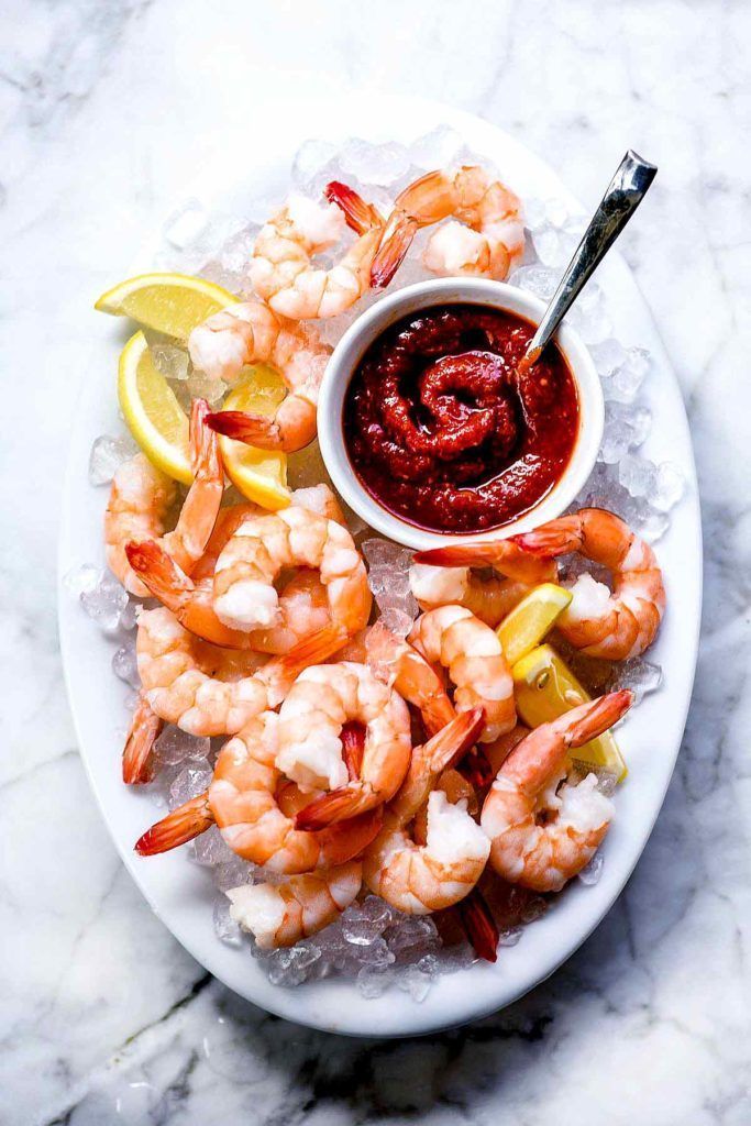 a plate with shrimp, lemon wedges and ketchup on it next to a bowl of sauce