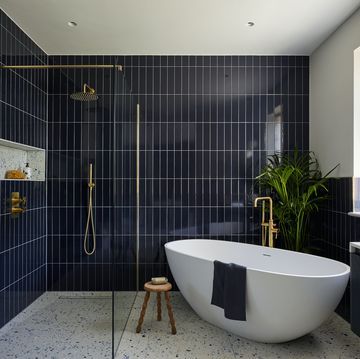 a bath tub sitting next to a walk in shower under a bathroom window with blue tiles on the walls