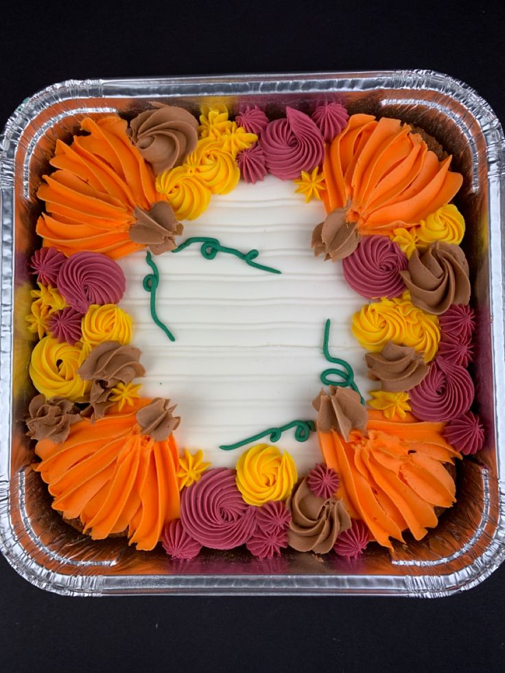 a cake decorated with orange, yellow and pink icing in a plastic container on a black surface