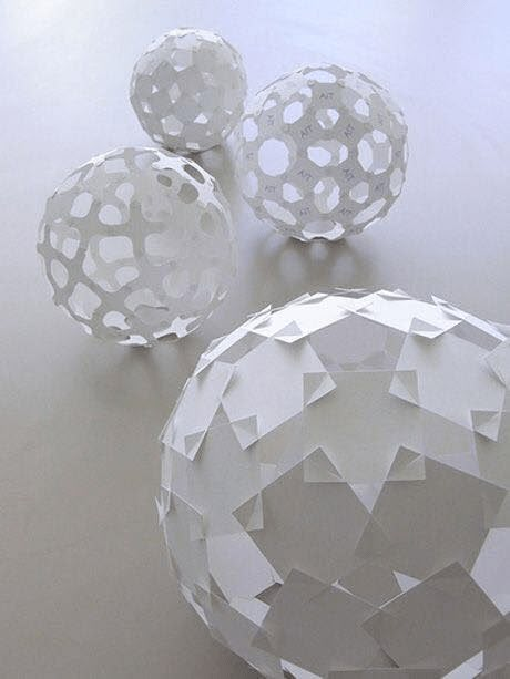 three white paper balls sitting on top of a table next to each other with holes in them