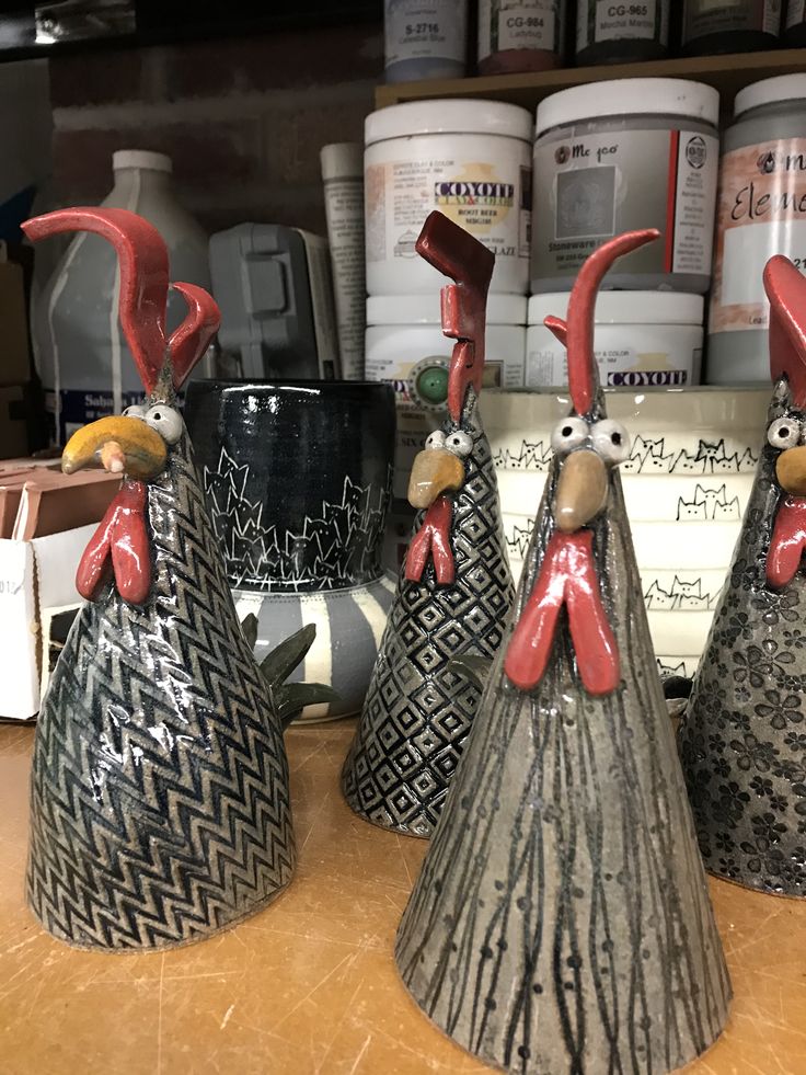 three ceramic roosters sitting on top of a counter next to paint cans and jars