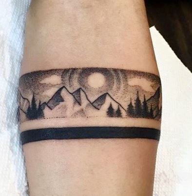 a man with a tattoo on his arm that has mountains and trees in the background