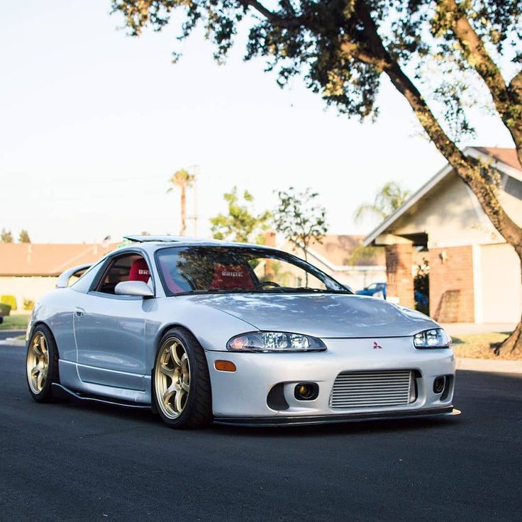 a white sports car parked on the side of the road near a tree and houses