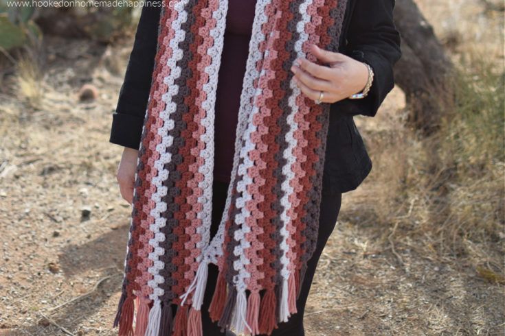 a woman wearing a red, white and black crocheted scarf standing in the desert