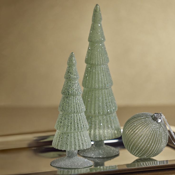 three glass christmas trees sitting on top of a table next to a silver ornament