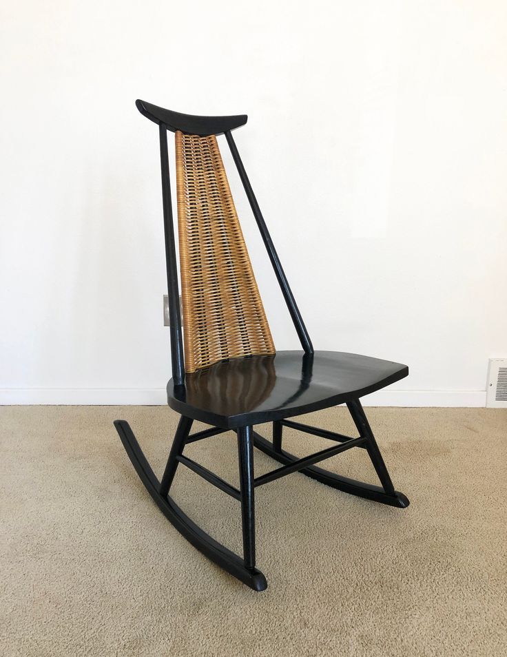 a black rocking chair with wicker seat on carpeted floor next to white wall