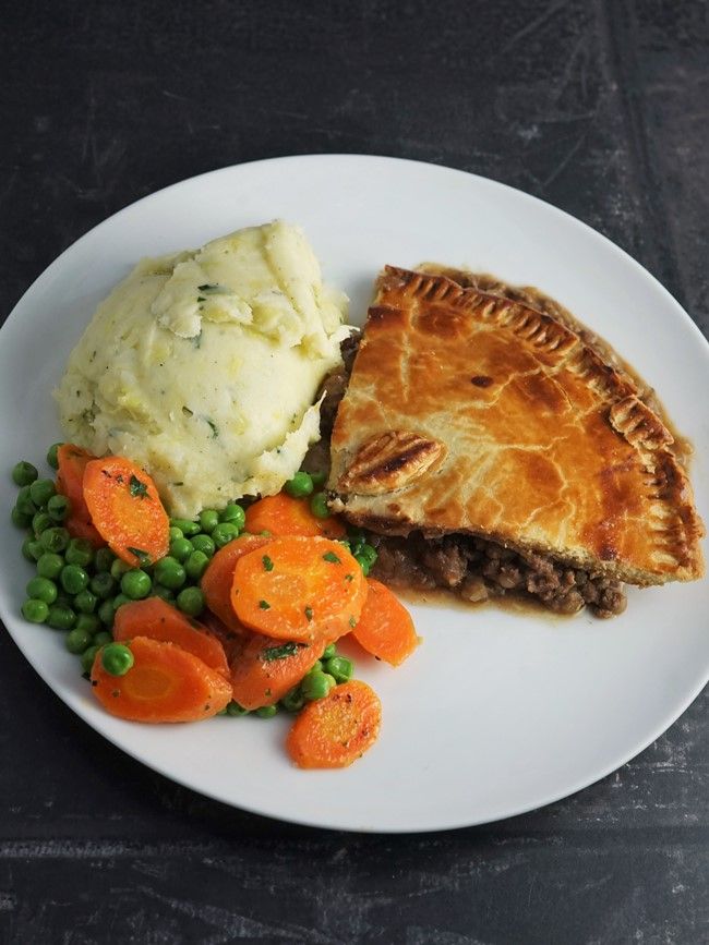 a white plate topped with meat, mashed potatoes and veggies next to a pie