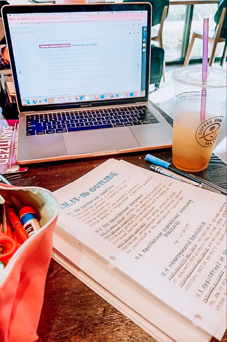 a laptop computer sitting on top of a wooden table next to a notebook and pen