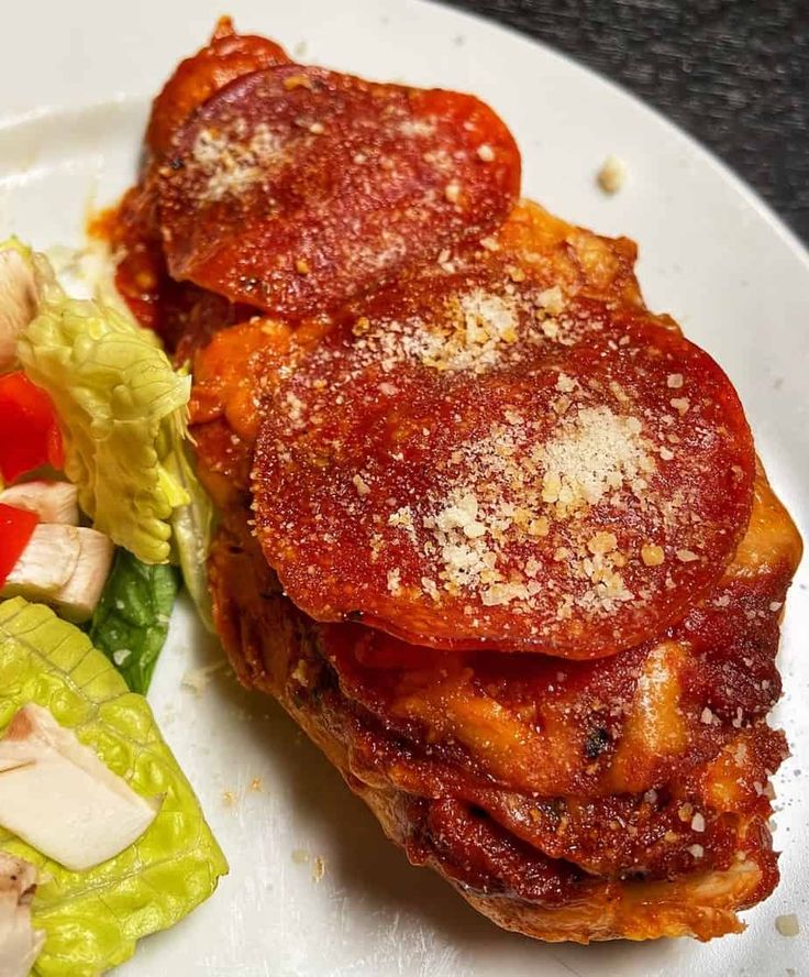 a white plate topped with meat covered in sauce next to a salad and lettuce