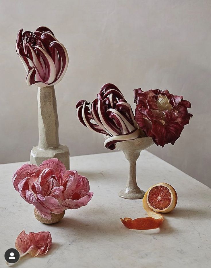 three vases with flowers and fruit on a white countertop next to each other