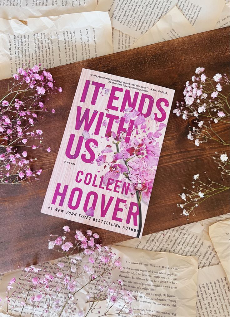 the book it ends with us by collien hoover sits on top of some flowers