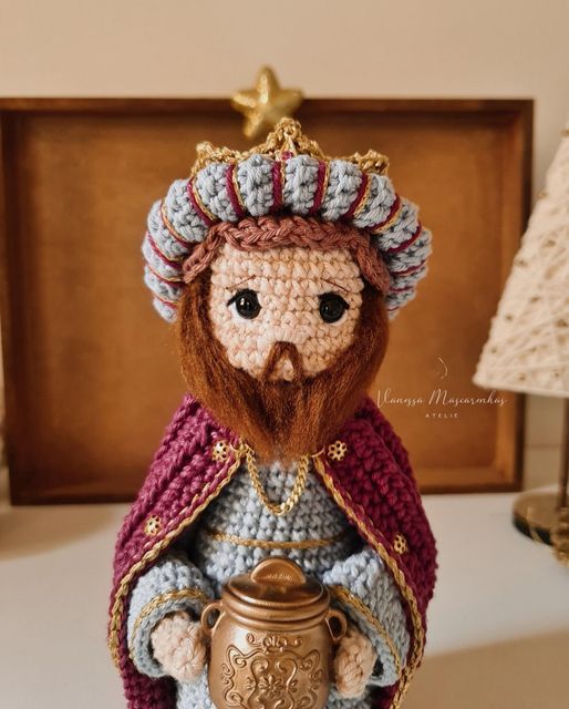 a crocheted figurine with a beard holding a golden urn in front of a wooden frame